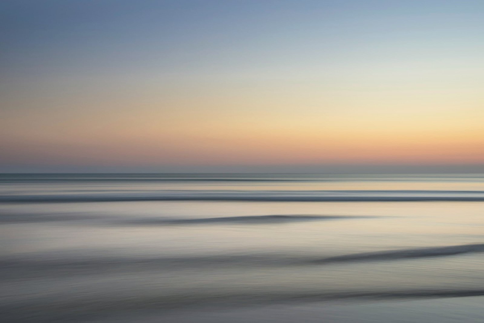 A calm sea at dusk, the low waves blurred into soft bands under a sky fading from blue to gold.